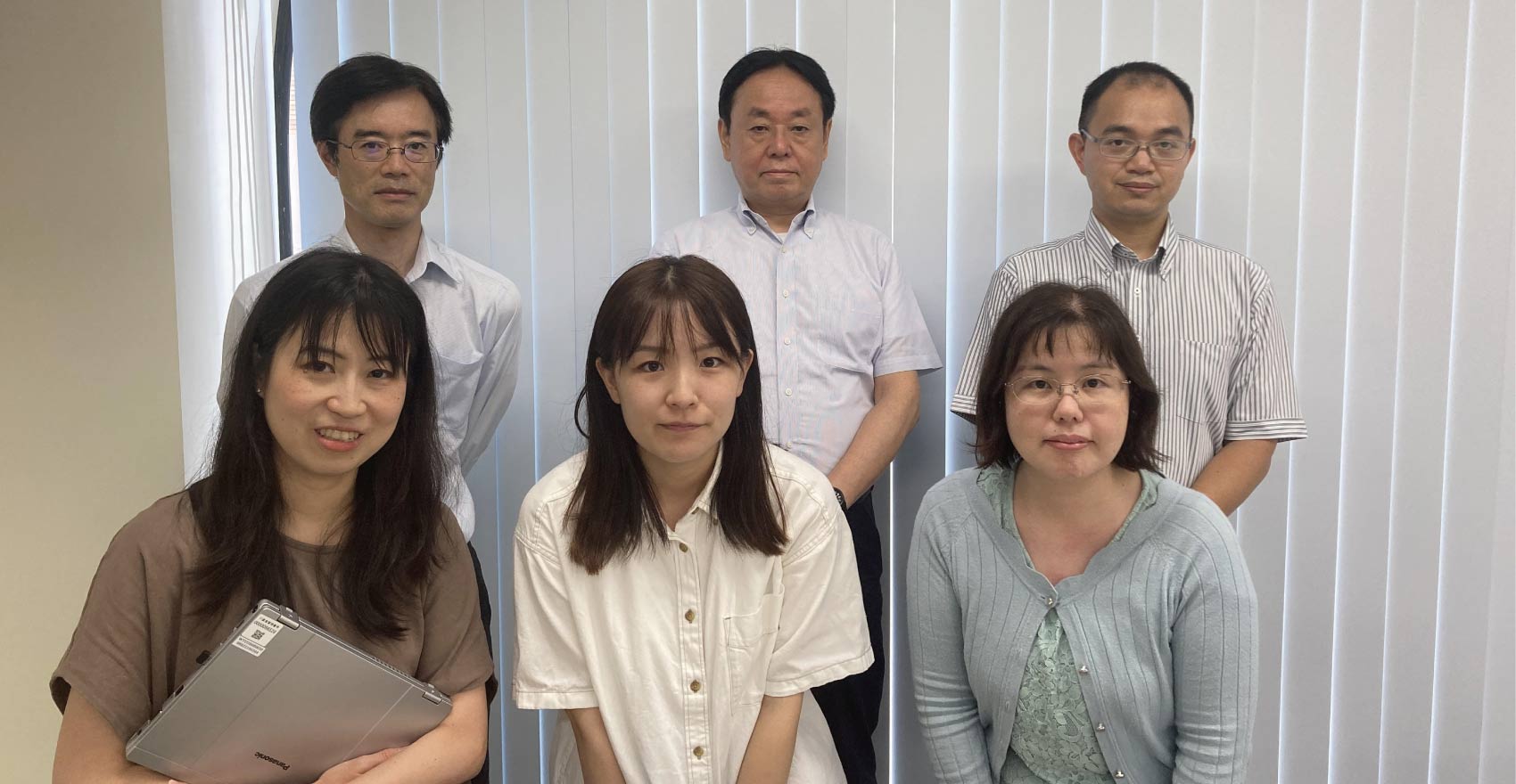 男性社員3名が後ろに立ち、女性社員3名が前にかがんで並ぶ形の集合写真
