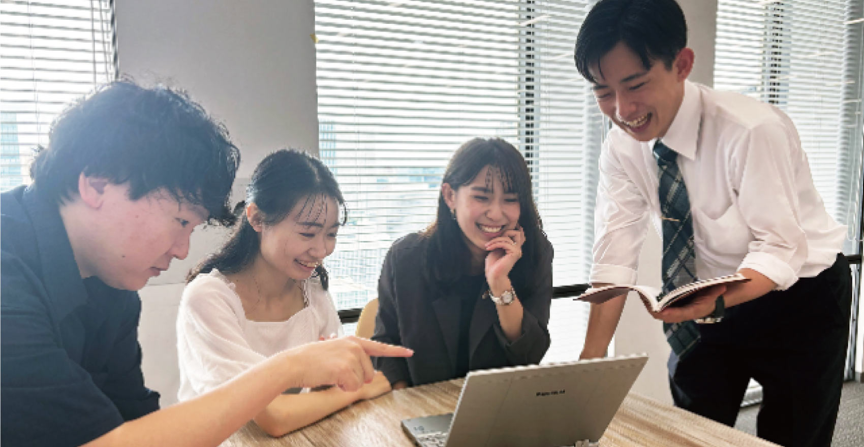男性社員2名と女性社員2名の4人が一つのノートパソコンを見ながら打ち合わせを行う様子