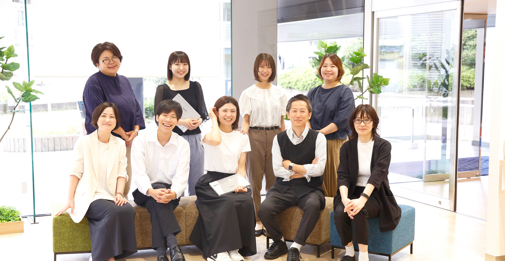 男性社員2名、女性社員7名の計9名が前後2列に並んだ形の集合写真