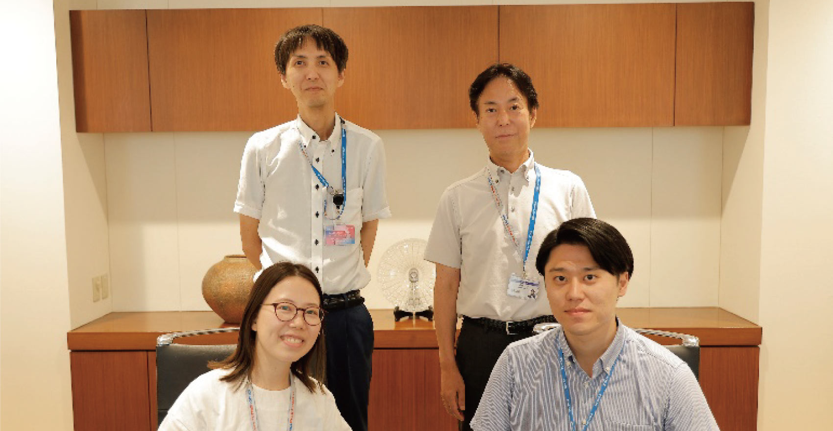男性社員3名、女性社員1名の計4名が前後2列に並んだ形の集合写真