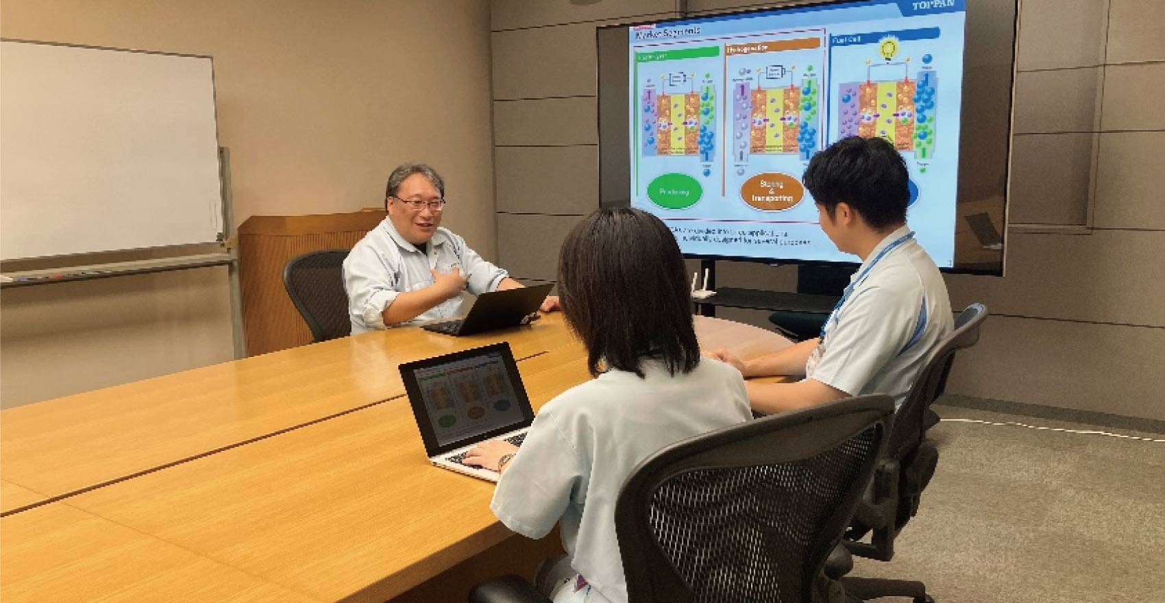 社員3名がノートパソコンとプロジェクターを使いながら打ち合わせを行う様子