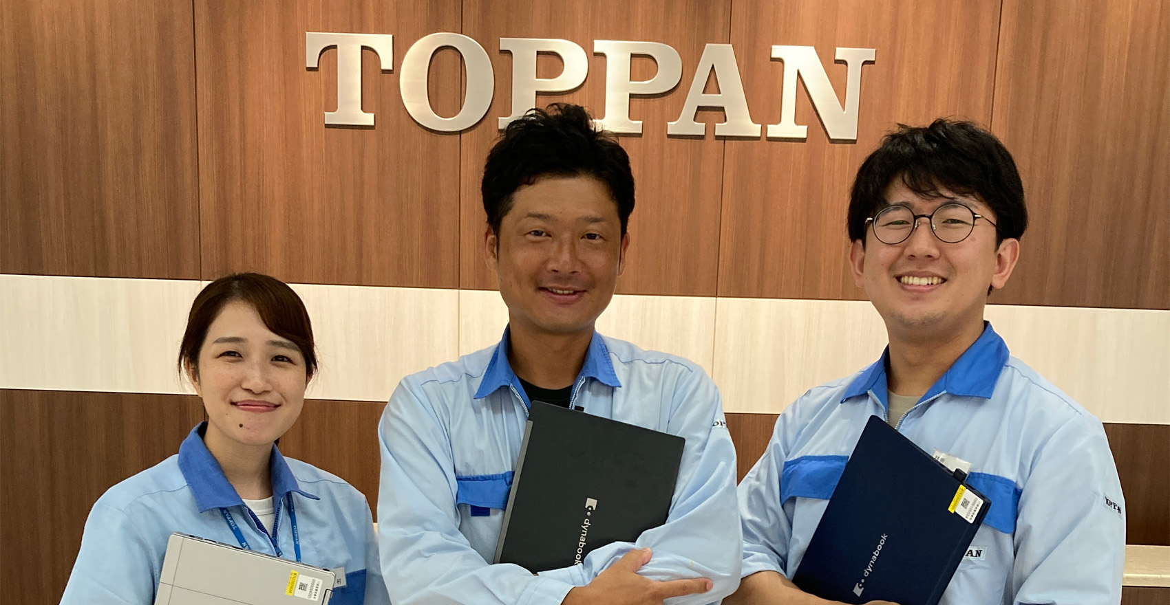 男性社員2名と女性社員1名が正面を向いて並んで笑顔をむける様子